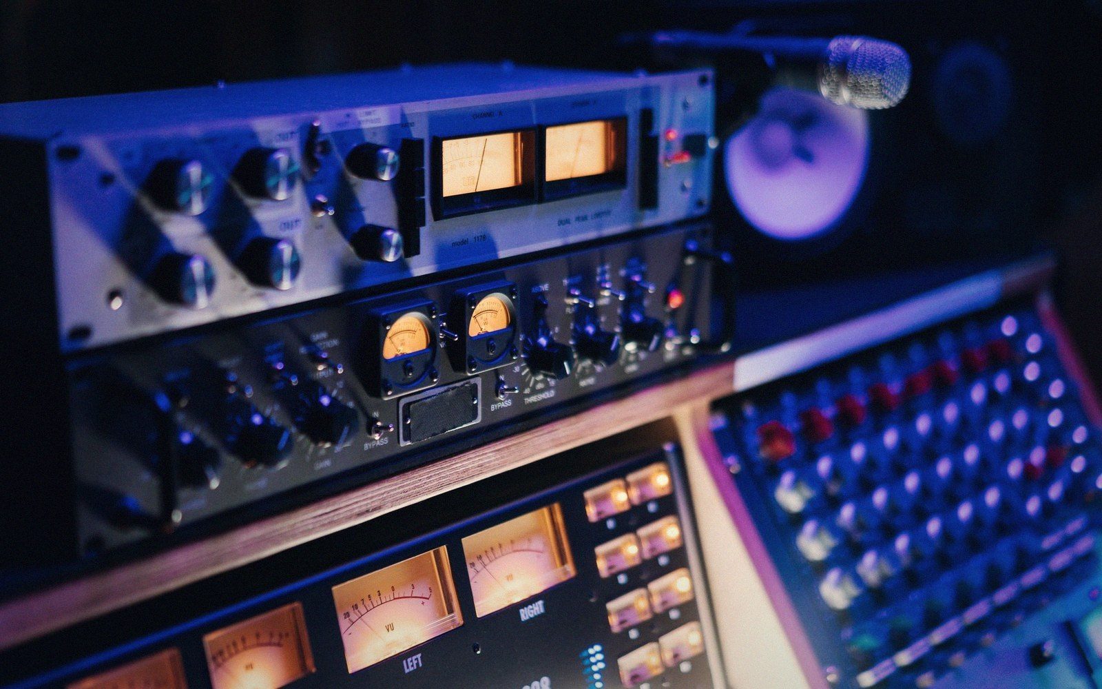 Nearfield studio monitors flanking a hardware rack in a dark production room, LED meters glowing green
